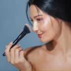 Beautiful woman with natural makeup glow, applying makeup with a brush. Perfect for beauty, cosmetics, and skincare promotions, highlighting natural beauty and high-quality products.